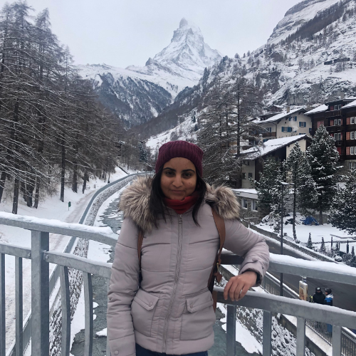 Sanskruti stood on a bridge over a snow covered road with trees and a mountain in the background