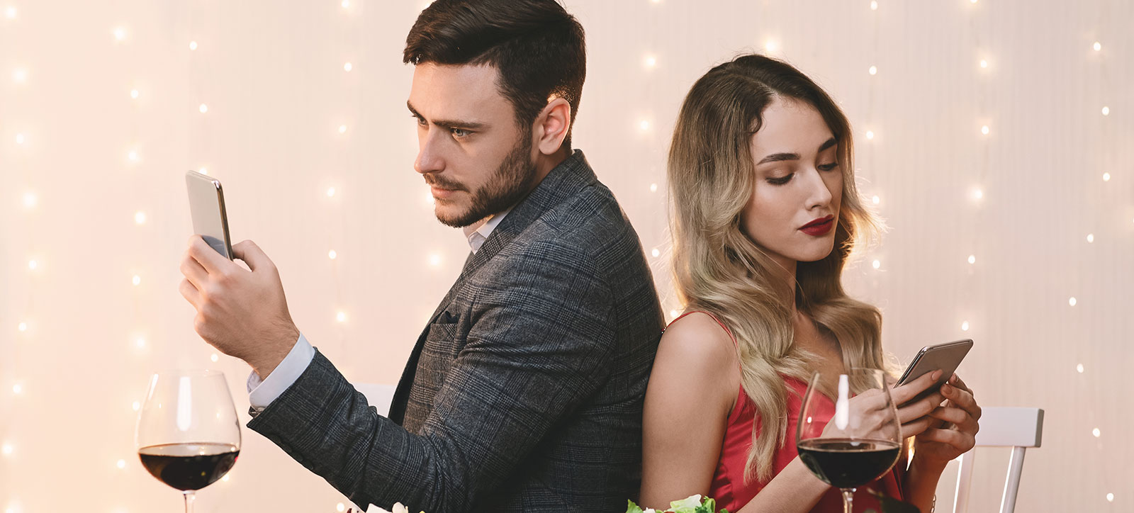 A couple on a date sit with their backs to each other, looking bored, as they each stare at their mobile phones.