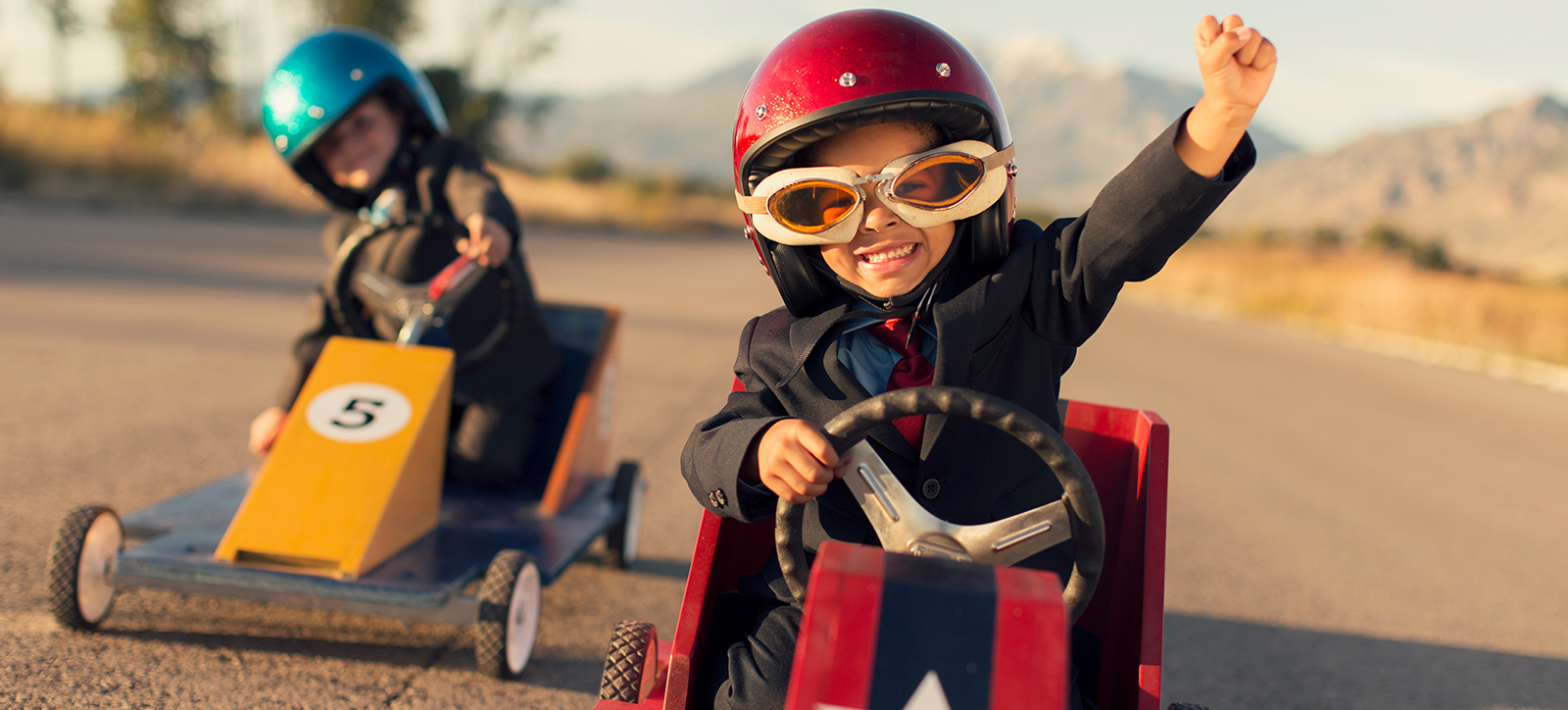 Two children in business suits drive go karts around a track, representing the race for competitive advantage between rival companies Two children in business suits drive go karts around a track, representing the race for competitive advantage between rival companies