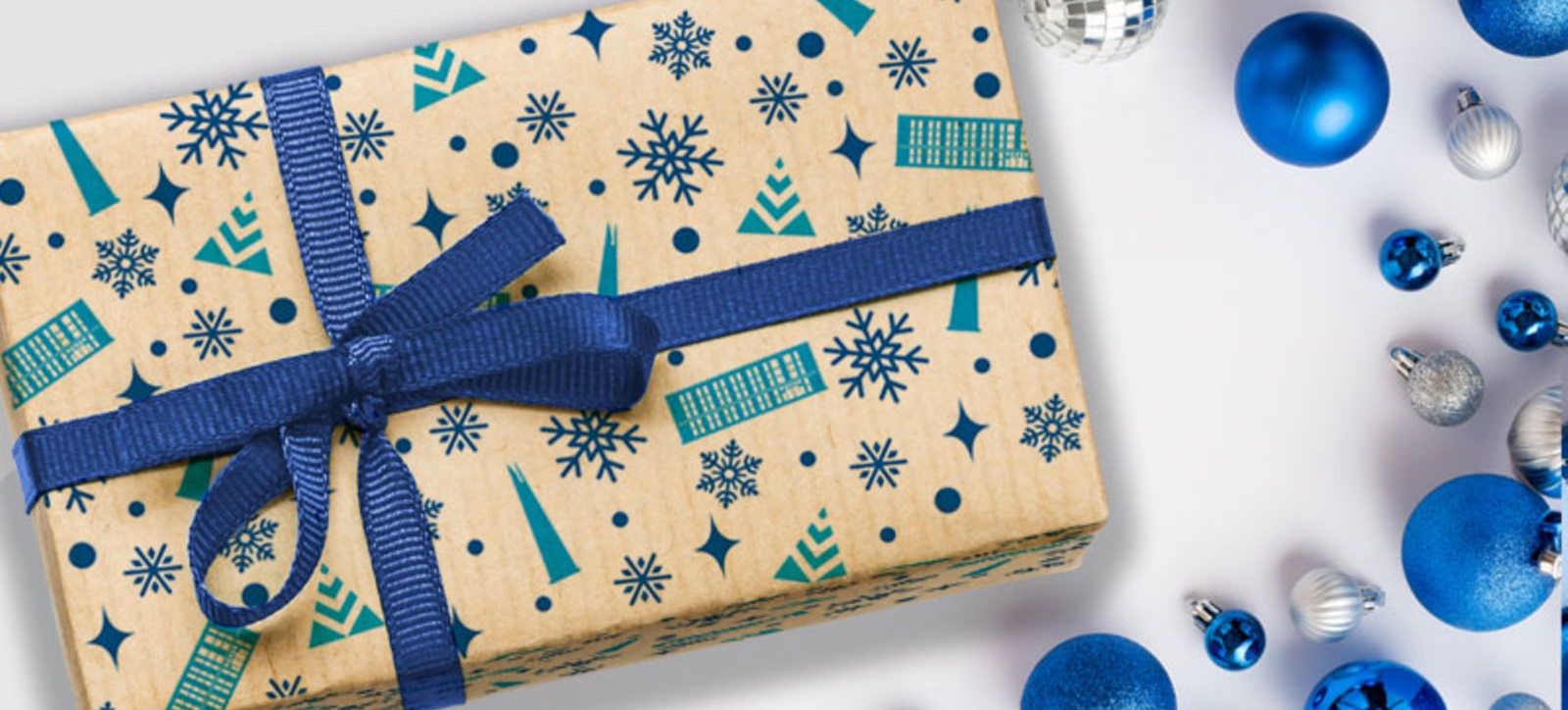 A Christmas present wrapped in Warwick Business School themed paper and a blue bow, surrounded by blue and silver baubles. A Christmas present wrapped in Warwick Business School themed paper and a blue bow, surrounded by blue and silver baubles.