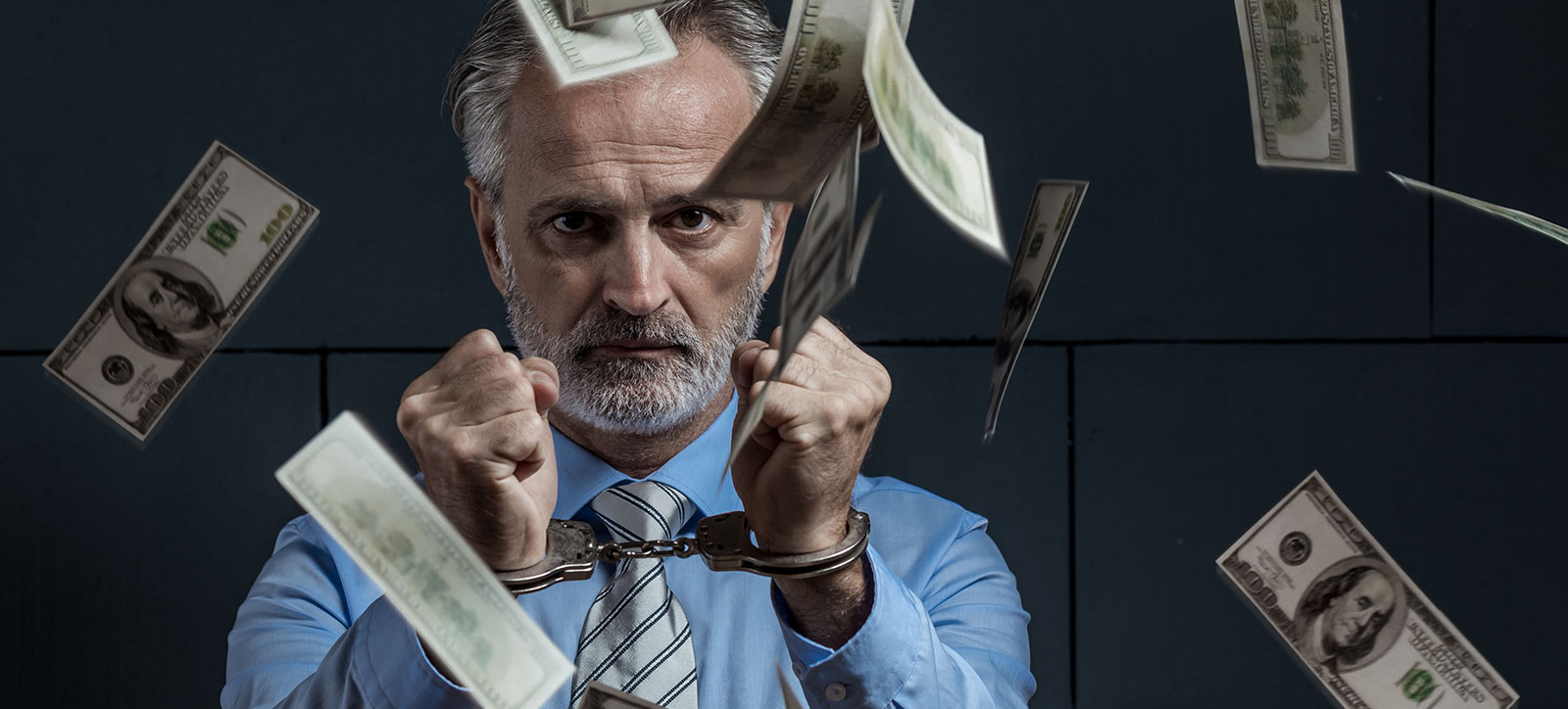 A businessman in a shirt and tie wearing handcuffs in a prison cell as dollar bills fall around him A businessman in a shirt and tie wearing handcuffs in a prison cell as dollar bills fall around him