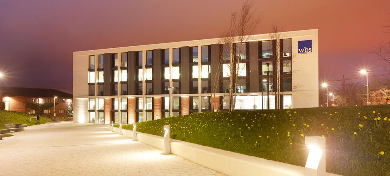 The main Warwick Business School building located in Coventry on the University of Warwick campus with a soft sunset in the background.