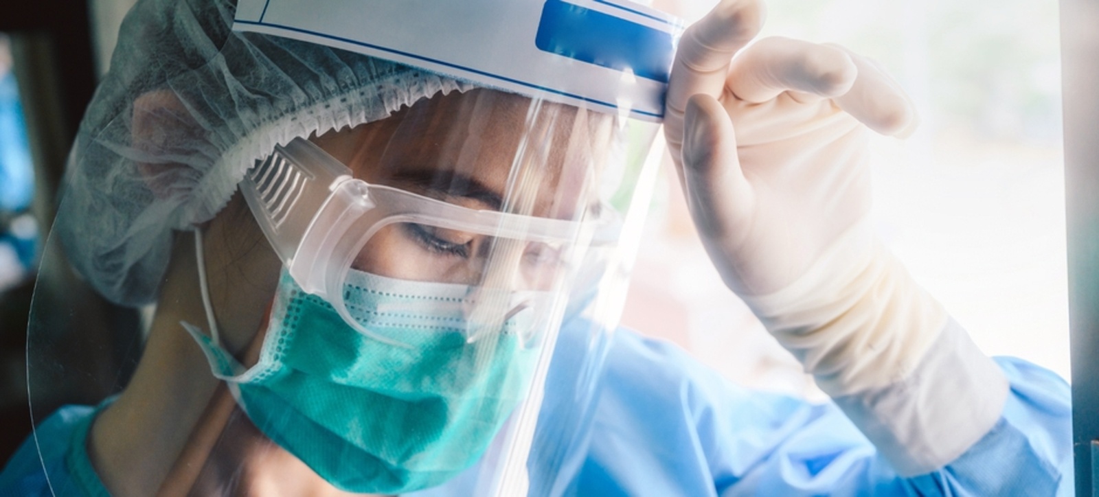 A female medical worker dressed in PPE holding her hand up to her forehead. A female medical worker dressed in PPE holding her hand up to her forehead.