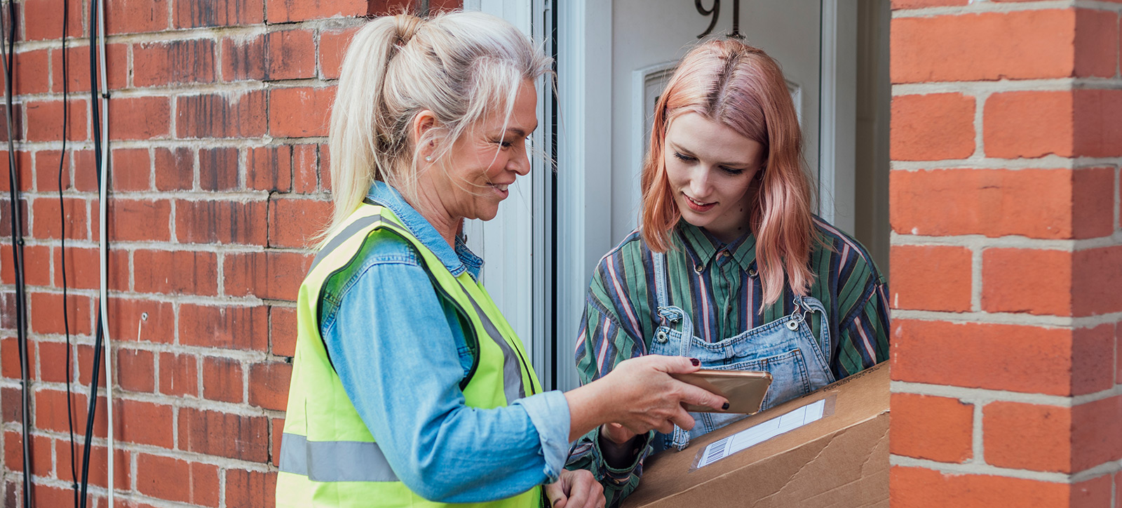 A postal worker delivers a parcel to a customer at the front door of her home. A postal worker delivers a parcel to a customer at the front door of her home.